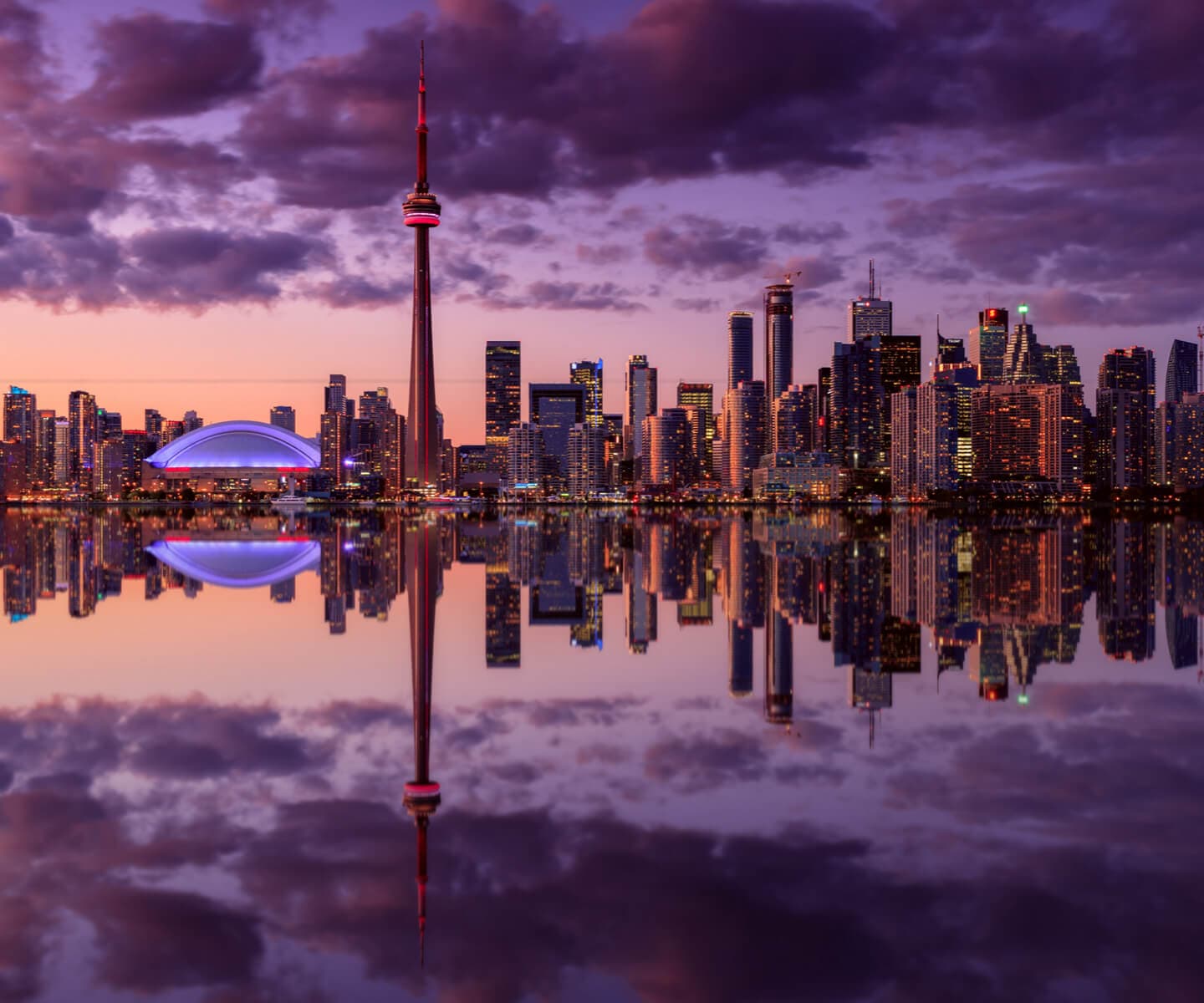 Silhouette de Toronto à la brunante, avec la Tour CN et le Rogers Centre, qui se réfléchit sur une eau calme