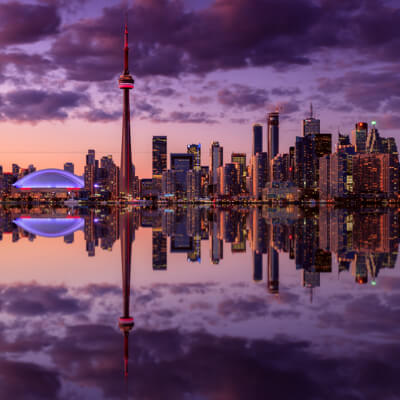 Silhouette de Toronto à la brunante, avec la Tour CN et le Rogers Centre, qui se réfléchit sur une eau calme