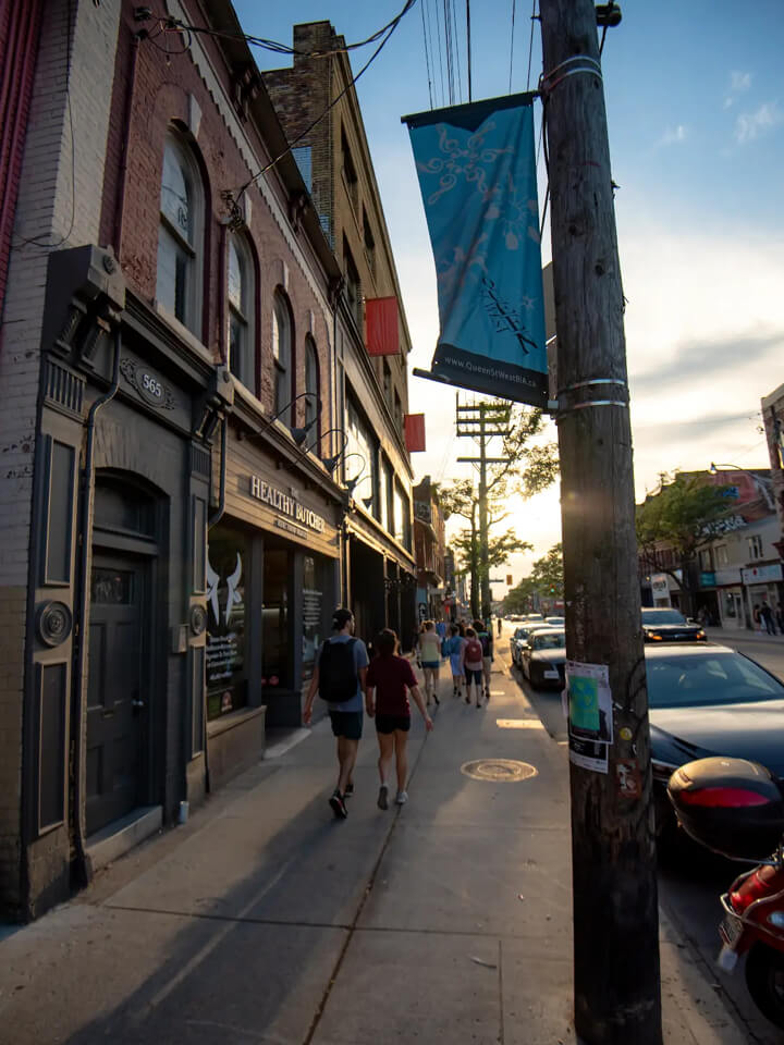 Gens marchant sur un trottoir bondé sur la rue Queen Ouest au coucher du soleil avec des enseignes néon brillantes